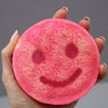 A vibrant pink scrub soap bar with a textured surface and embossed smiley face from happy scrub soap bars strawberry guava