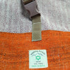 Orange hemp trekking rolling backpack with gray plastic buckle and white label showing hemp materials and nepal origin