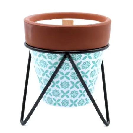 A teal and white ceramic herb garden soy wax rosemary candle holder with a terracotta rim on a black metal stand