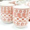 White ceramic mugs with red floral and geometric patterns as part of an herbal teapot set amber design