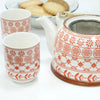 White ceramic herbal teapot with orange floral and geometric patterns and a built-in metal strainer