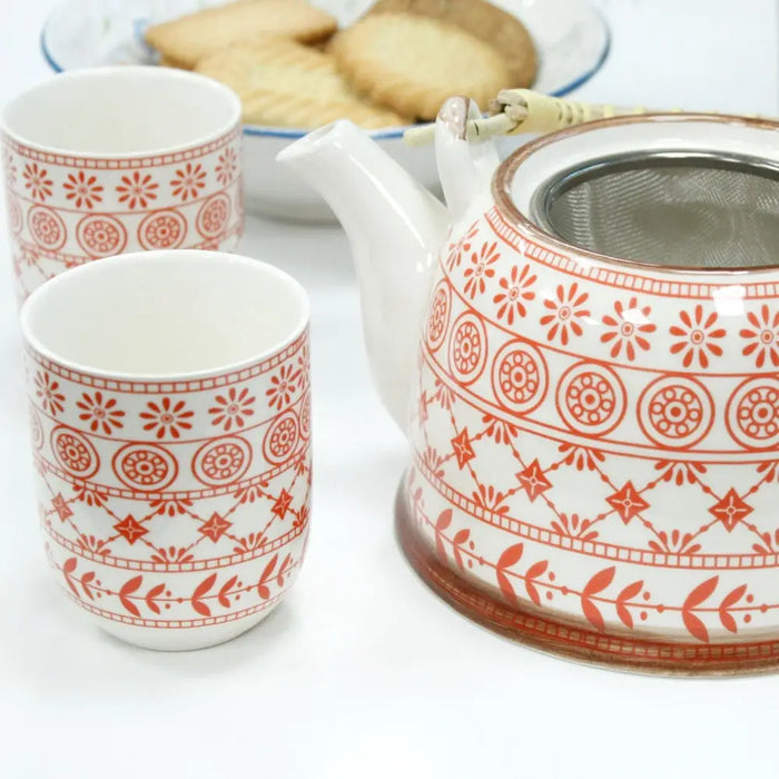 White ceramic herbal teapot with orange floral and geometric patterns and a built-in metal strainer