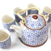 White ceramic herbal teapot set with blue geometric floral pattern and woven bamboo handle and brown glazed rim