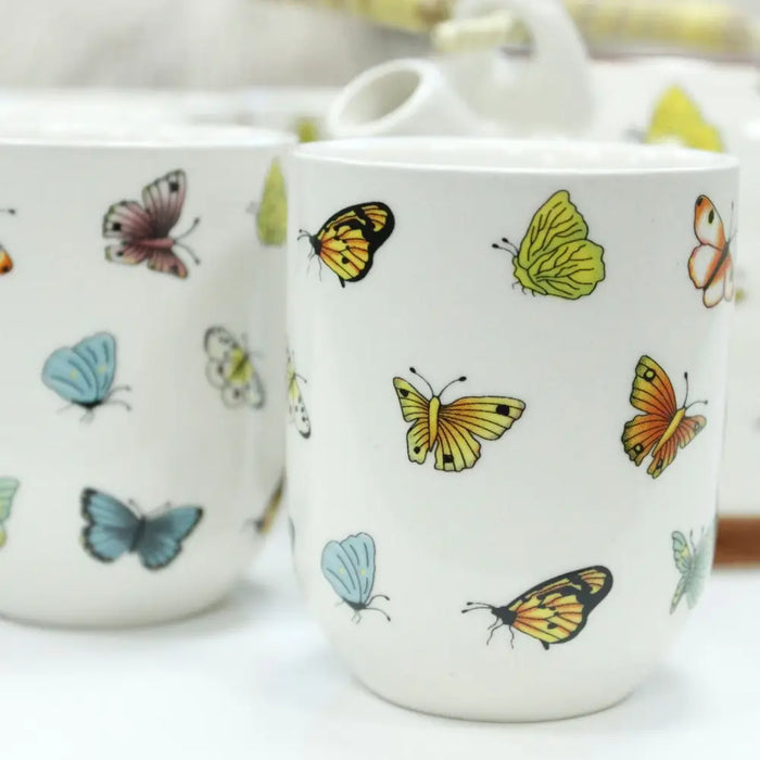 White ceramic mug with colorful yellow orange blue and pink butterflies as part of a herbal teapot set design