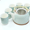 A ceramic herbal teapot set with a green mosaic pattern on white porcelain and a woven bamboo handle
