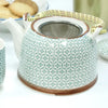 A white ceramic teapot with green geometric patterns and brown rim accents featuring a bamboo handle