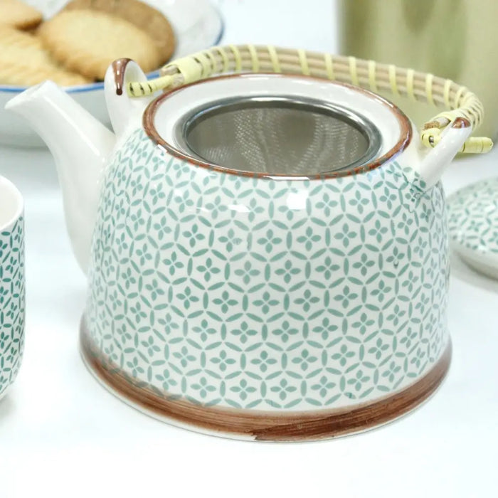 A white ceramic teapot with green geometric patterns and brown rim accents featuring a bamboo handle