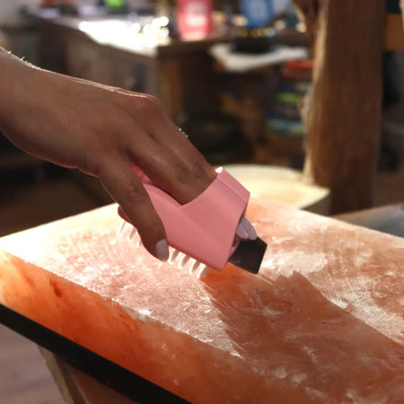 Pink plastic block cleaning brush with white bristles used on pinkish-orange himalayan salt plate for salt block cleaning
