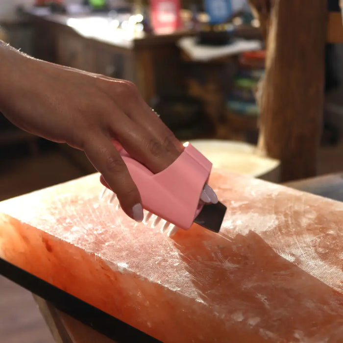 Pink plastic block cleaning brush with white bristles used on pinkish-orange himalayan salt plate for salt block cleaning