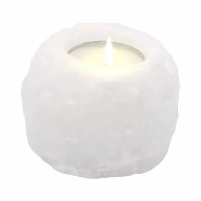 A white himalayan salt tealight holder made of textured crystal rock with a lit candle inside