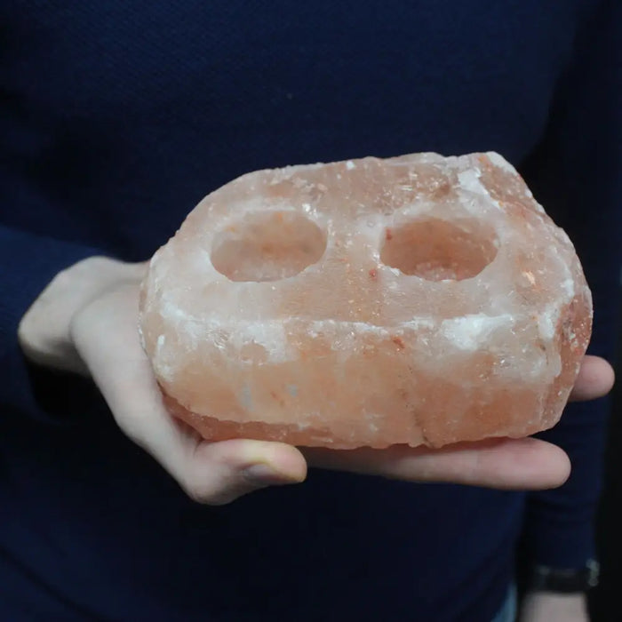 A pinkish-orange himalayan salt candle holder with two circular holes designed as tealight holders