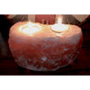 A heart-shaped pinkish orange himalayan salt candle holder with two lit tealight holders carved in it