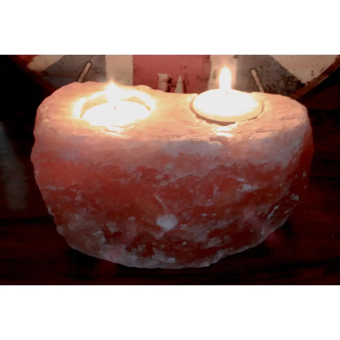 A heart-shaped pinkish orange himalayan salt candle holder with two lit tealight holders carved in it