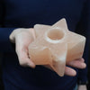 A pale pink himalayan salt star-shaped tealight holder with a smooth crystalline texture and central candle hole