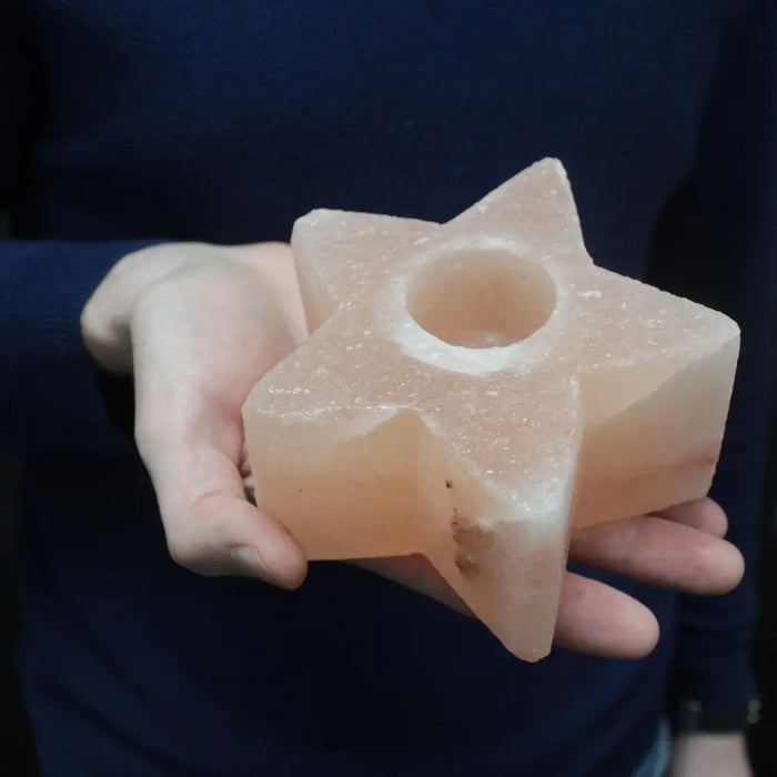 A pale pink himalayan salt star-shaped tealight holder with a smooth crystalline texture and central candle hole