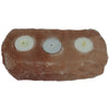 A rustic rectangular himalayan salt candle holder with three circular indentations holding white tealight holders