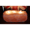 A rustic orange-pink himalayan salt candle holder with three lit tealight holders in natural carved indentations
