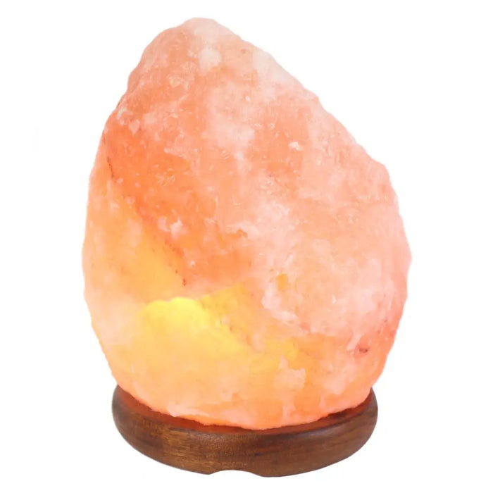 A warm glowing pink himalayan salt lamp with natural crystalline texture on a dark wooden base weighs 3-5kg