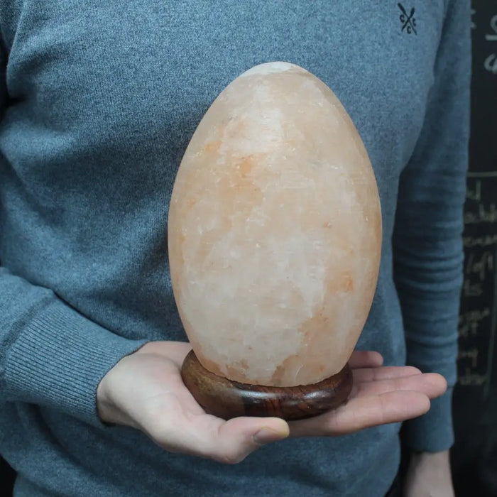 A peach-hued himalayan salt lamp egg weighing 3kg with smooth surface and polished wooden base showing hygroscopic properties