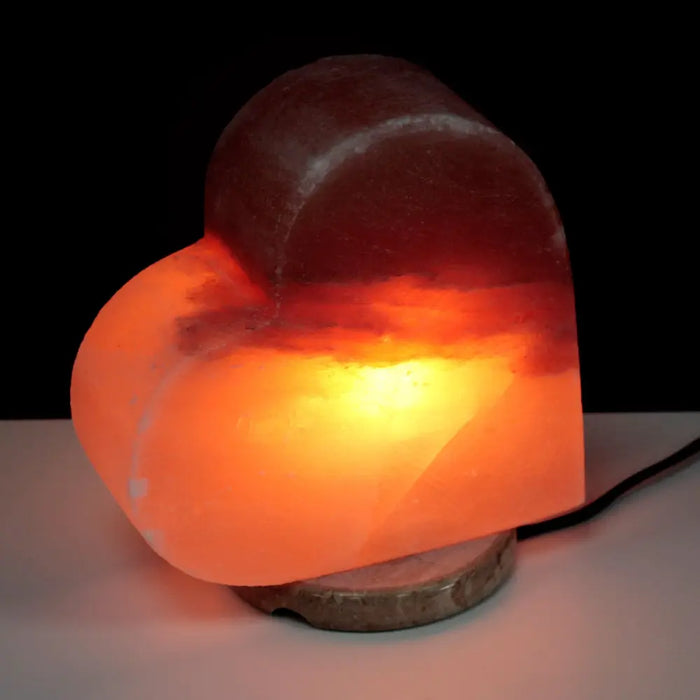 A himalayan salt lamp heart glowing warm orange made from translucent salt on a rustic stone base showing hygroscopic properties