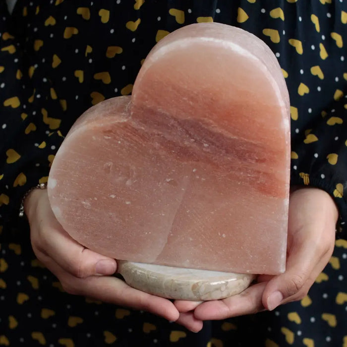 A translucent pink himalayan salt lamp heart with a smooth natural stone base showing hygroscopic properties