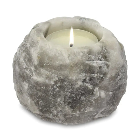 A rustic grey stone himalayan salt tealight holder with a textured surface holding a lit white tea light candle