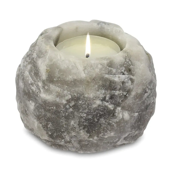 A rustic grey stone himalayan salt tealight holder with a textured surface holding a lit white tea light candle