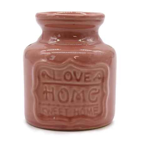 A glossy pink terracotta home oil burner with a rounded neck and embossed love home sweet home label