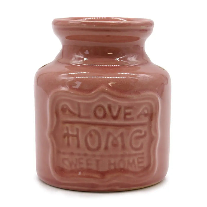 A glossy pink terracotta home oil burner with a rounded neck and embossed love home sweet home label