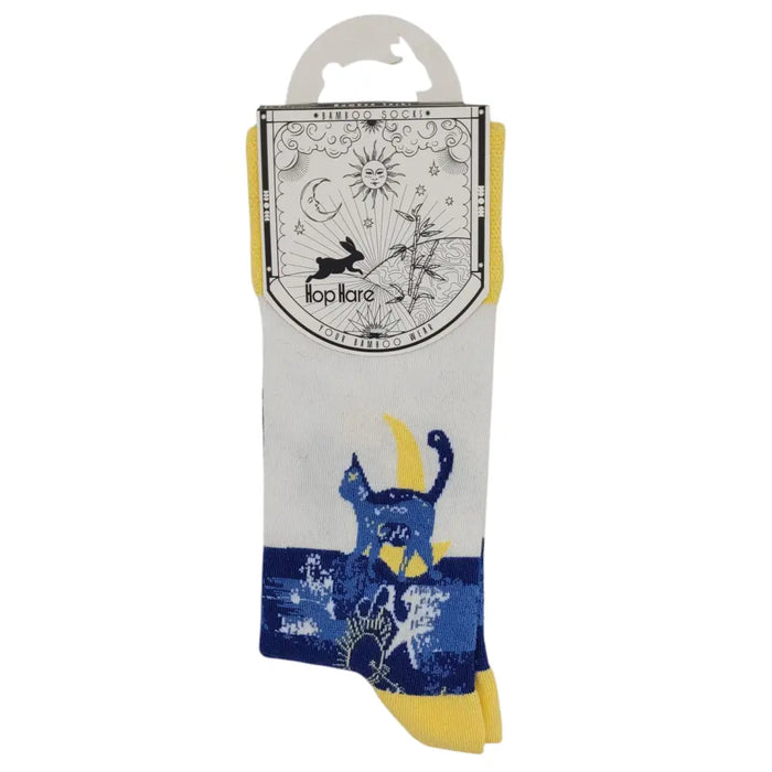 A pair of white bamboo socks with blue cat design yellow accents and whimsical celestial packaging illustrations