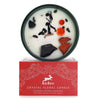 A white crystal floral candle in a dark green container with black and orange gemstones from hop hare crystal magic