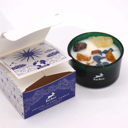 A dark green glass jar candle with white wax, dried botanicals, and crystals branded hopplare hop hare crystal magic flower