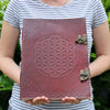 Huge burgundy leather book with embossed flower of life design and ornate metal clasps measuring 13 by 10 inches