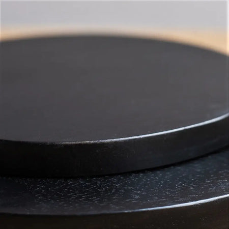 Black circular coaster with smooth matte finish and raised edge on ian snow dark wood cheese board