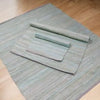 Gray textured handloom cotton rug with rolled-up rectangular mats placed on top in charcoal color