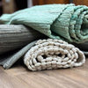 A soft mint green indian handloom cotton rug with woven rope texture on top of a rolled beige braided mat