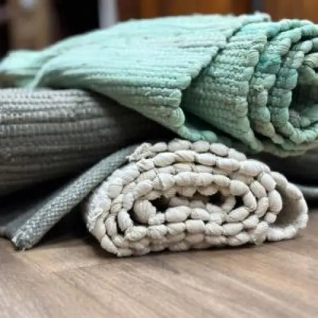 A soft mint green handloom cotton rug with woven rope pattern layered on a rolled beige braided indian handloom mat