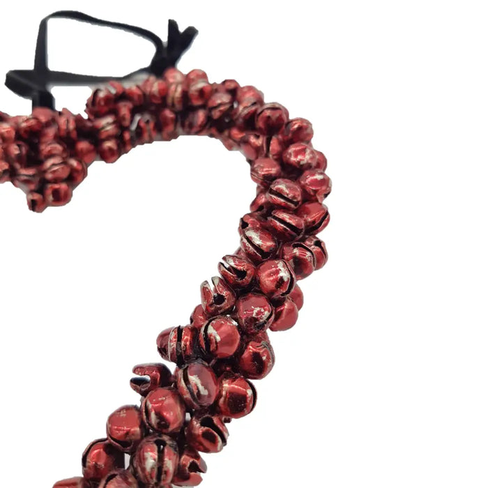 A heart-shaped wall hanging of small shiny red metal jingle bells with a black ribbon loop at the top
