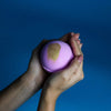 A jumbo bath bomb pink charlotte in soft lavender with gold foil held in hands featuring sodium lauryl sulfoacetate and peel oil