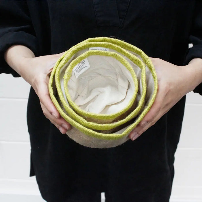 Set of three nested handwoven jute baskets with lime green rims and cream interior linings for storage use