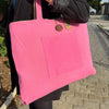 A vibrant pink jute and cotton tote bag with a front pocket and wooden button closure