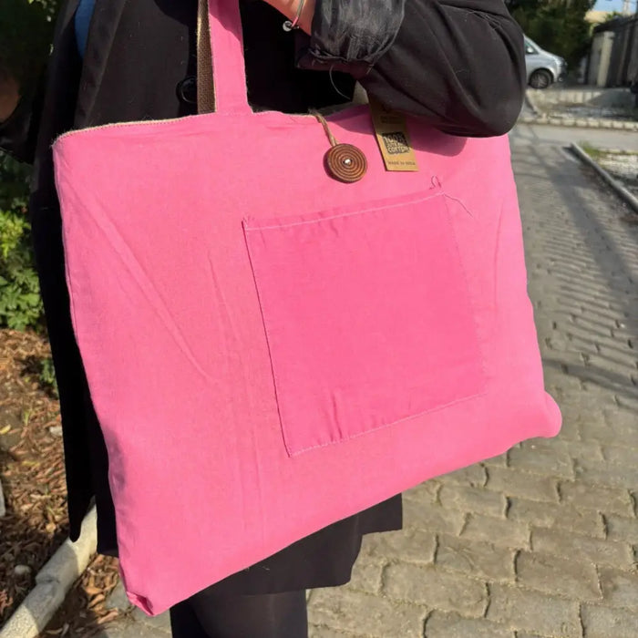 A vibrant pink jute and cotton tote bag with a front pocket and wooden button closure