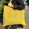 A mustard-yellow jute and cotton tote bag with a front patch pocket and wooden button closure