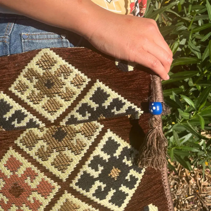Brown kilim summer messenger bag with geometric patterns in beige black rust and a blue beaded tassel accent