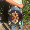 A dark navy kilim summer messenger bag with a dark blue woven body, orange green cream geometric pattern, black tassels, and beads