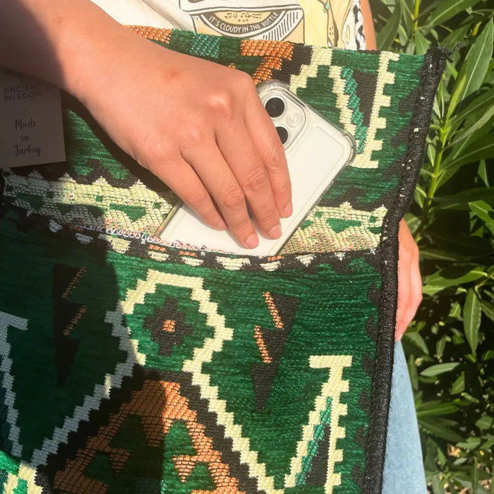 Green black and cream geometric woven kilim summer messenger bag with hand holding white smartphone inside