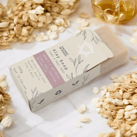 A rectangular pale beige kaolin clay soap bar wrapped in white and mauve paper with leafy line art packaging