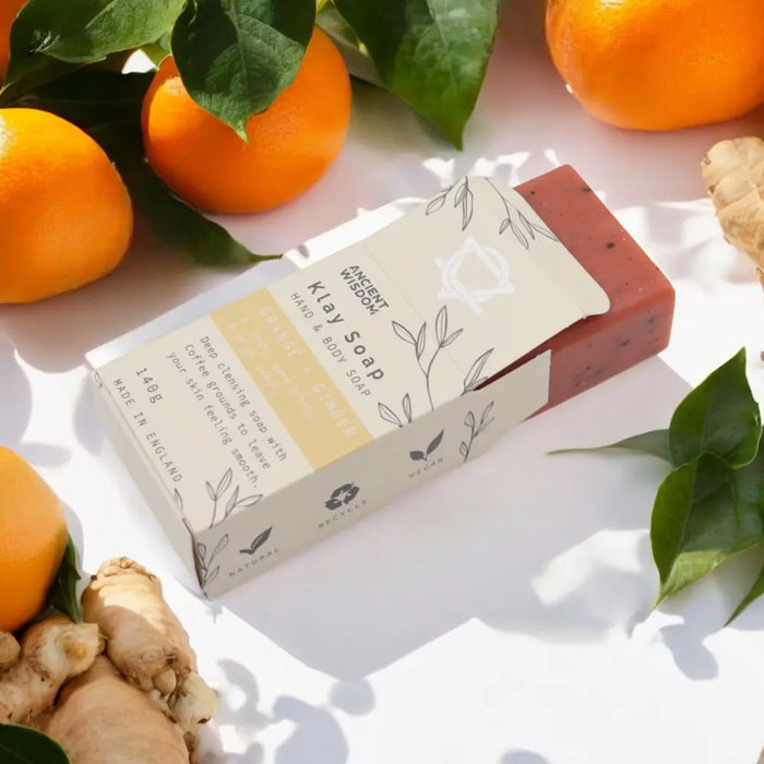 A rectangular reddish-brown clay bar soap with coffee grounds in a white box with botanical line art for cleansing