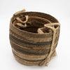 A rustic woven seagrass basket with brown tones and dark stripes featuring a sturdy rope handle and banana leaf accents