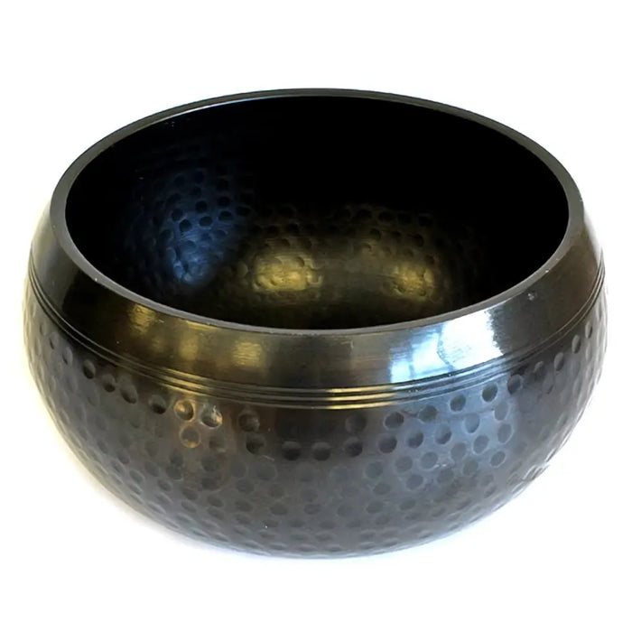 Large black beaten brass singing bowl with hammered metal texture and smooth reflective rim for sound therapy